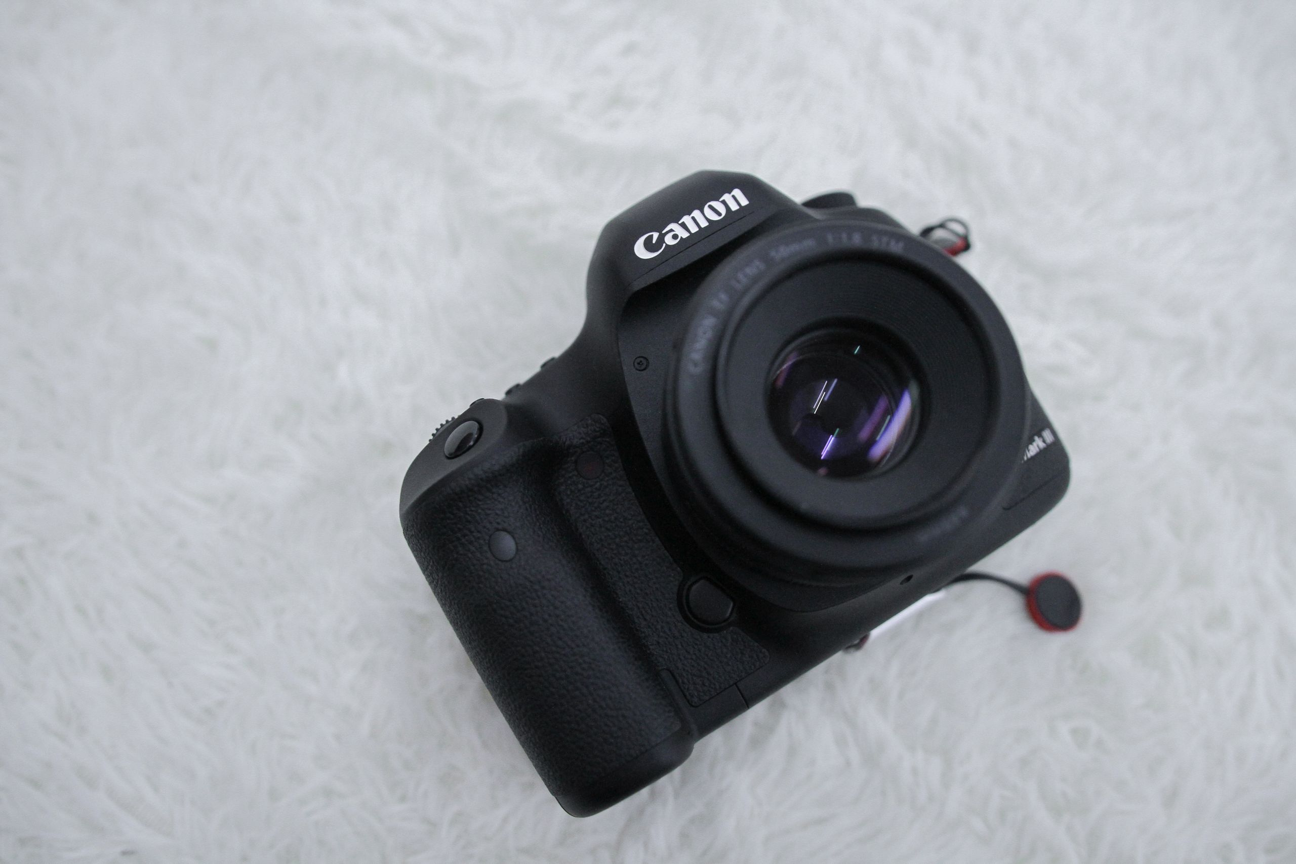 Canon DSLR camera featuring lens and design on a white fluffy surface, close-up shot.